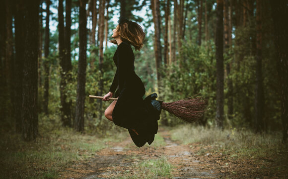 Young beautiful and mysterious Witch woman Flying on the Broom in woods. Levitation, a witch on a broom, free space. Halloween holiday, magic