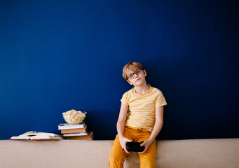 Blonde schoolboy boy plays video games, holds a gamepad, eats popcorn instead of learning lessons...