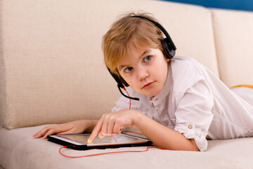 A boy with glasses and headphones is learning lessons with a tablet and books. Home distance learning online