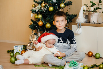 A little boy and his brother play with gifts under a festive Christmas tree. Happy Christmas and New Year celebrations