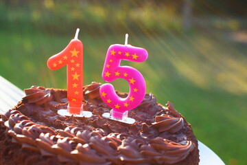 Brown chocolate anniversary or birthday cake with number 15 candles on it outdoors in sunlight.
