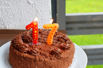 Brown chocolate anniversary or birthday cake with number seventeen 17 candles on it outdoors in sunlight.
