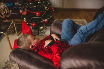 A boy with blond hair against the background of a Christmas tree lies on a sofa and dreams of the best Santa Claus gift