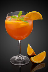 Glass of orange cocktail decorated with orange at black background.