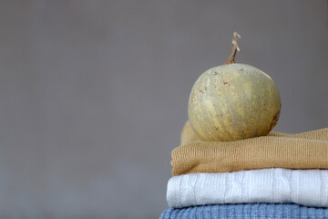 Stack of sweaters and small pumpkin. Selective focus.