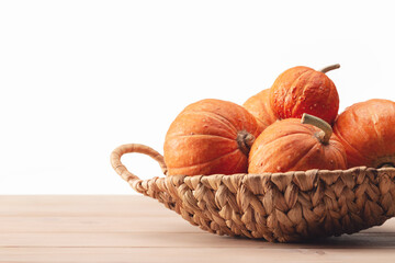 Orange round pumpkins in wicker basket on light wooden table. Copy space. Happy Halloween.