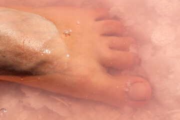 Woman leg foot fingers close-up in pink salt flakes top view under pink water surface. Healthy spa procedures on Syvash resort, the Putrid Sea or Rotten Sea, Ukraine