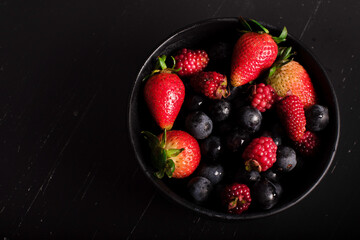 Frutos rojos fresas y uvas sobre fondo negro vista superior.