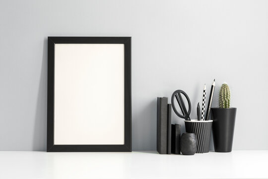 Picture frame and black supplies at home office workplace on a grey background. Mockup. Creative desk.