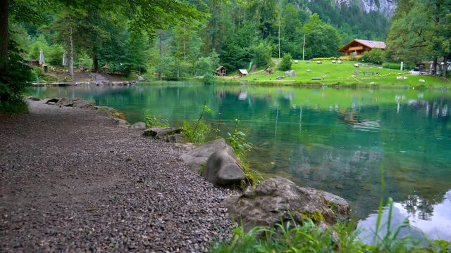 This is a close shot of Blausee. I&acute;m walking along side it and a butterfly is flying in front of me. You can also see fish swimming in the water.In the background is a mountain and a lodge.