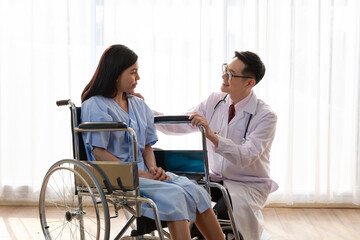 The doctor checked the patient's fever and explain treatment the sick patient to sitting wheelchair. Doctor make routine health check with patient on wheelchair in hospital ward. Healthcare concept.