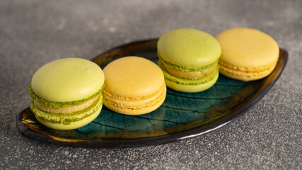 Close up of tasty piled yellow and green macaroons on beautiful green leaf plate. Pistachio and marakuja cakes