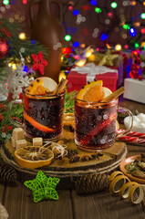 Mulled wine with orange slice, cinnamon stick on the background of festive garland lights. Dark style