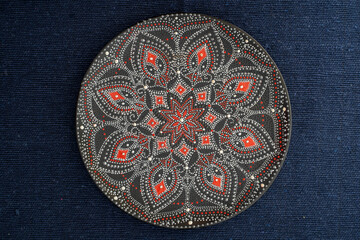 Decorative ceramic plate with black, red and golden colors, painted plate on background of blue fabric, dot painting