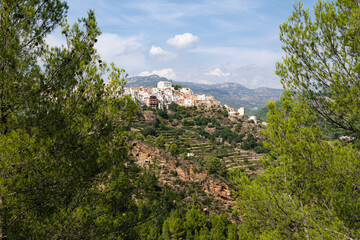 Among the trees a view of the village Lucena del Cid surrounded by nature on a day with blue sky and clouds, Castellon, Spain