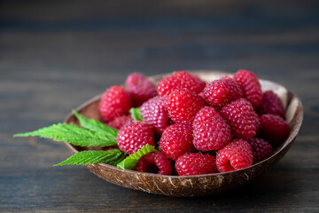 Harvest of ripe farm raspberries in coconut plate on the wooden table background. Close up