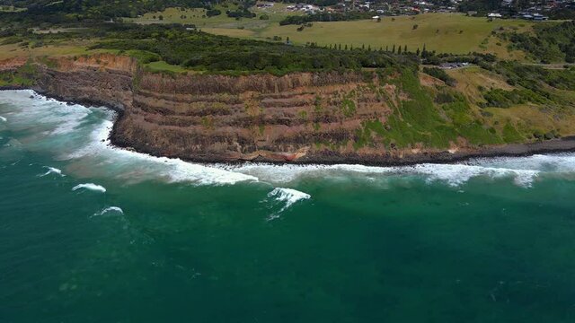 Foamy Waves Crashing Against The Coastal Cliffs - Lennox Point Headland In Summer - Pat Morton Lookout In Lennox Head, New South Wales, Australia. - aerial pullback shot