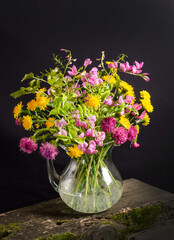 Lush bouquet of wild flowers in a vase on a black background in dark style, still life
