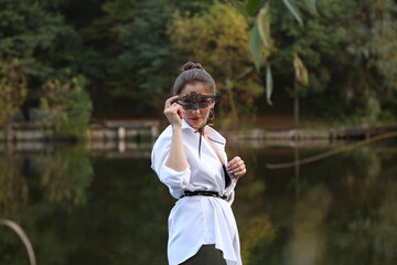 Woman with mask on her face in white shirt near the lake