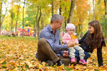 Mom, dad and daughter are playing on autumn leaves