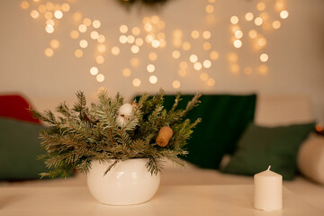 A white candle decorated with fir branches and red glass balls standing on a wooden table with a linen napkin