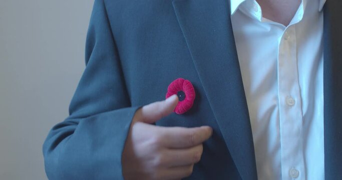 A Person with a remembrance day poppy flower on a black suit on the left side
