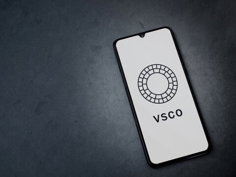 Lod, Israel - July 8, 2020: VSCO - Photo and Video Editor app launch screen with logo on the display of a black mobile smartphone on a dark marble stone background. Top view flat lay with copy space. 