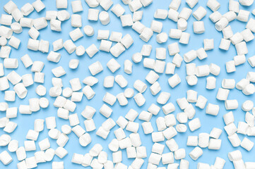 White sweet marshmallows on blue background flat lay top view copy space. Winter or autumn food concept, New Year's or Christmas sweetness, candy, dessert. Marshmellow texture. Minimalistic style