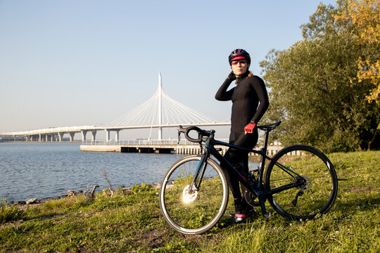 Portrait of a woman cyclist on the shore of the Gulf of Finland against the background of a cable-stayed bridge. Outdoor cycling. Morning workout.