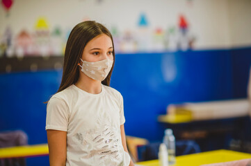 Elementary schoolchild wearing a protective face masks in the school. Education during epidemic.