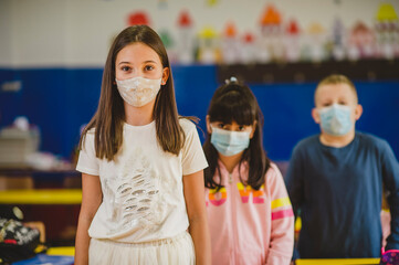 Elementary schoolchildren wearing a protective face masks  in the classroom. Education during epidemic.