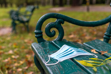 Used disposable face mask on bench in park. Environmental damage and pollution during coronavirus covid-19 pandemic in city