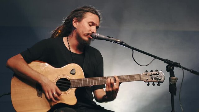 Male musician playing acoustic guitar. Guitarist plays in classical guitar on stage in concert . Rock music band .