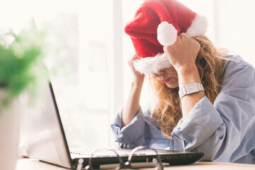 woman with santa claus hat and computer with expression of tired or overwhelmed
