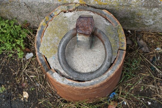 round concrete setting for metal mooring ring on pavement with weeds 