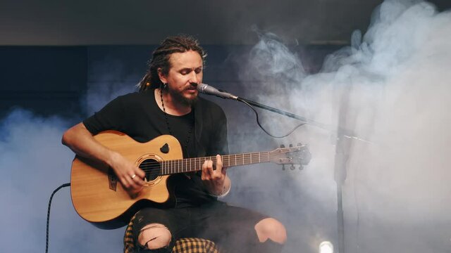 Male musician playing acoustic guitar. Guitarist plays in classical guitar on stage in concert . Rock music band .