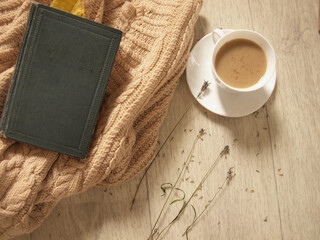 Hot coffee, lavender, warm sweater and book on wooden background