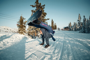 Woman making hand stand on ski resort with snowboard on her legs. Circus girl snowboarding. Crazy...