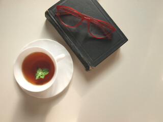 Cup of tea with mint, old book and glasses.