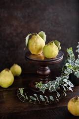 Large quince fruits with foliage on a stand on a brown wooden table. Harvest of autumn fruits.