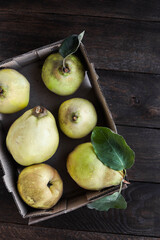 Large quince fruits in a cardboard box on a brown wooden table. View from above.