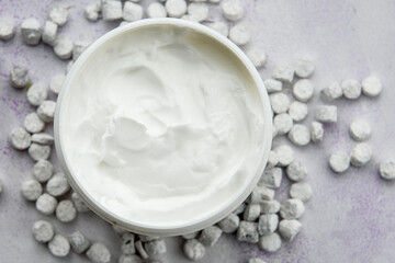 Close-up of a smooth moisturizer in a plastic jar on a blue background with white small stones on top. The concept of skin care.
