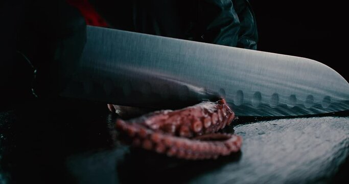 Chef cortando suavemente un pedazo de pulpo, ingrediente para cocinar comida japonesa. Tent&aacute;culos de pulpo fresco cortados suavemente por un chef  en una tabla negra.  4K
