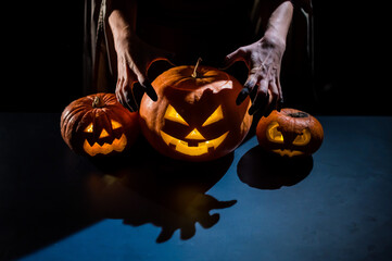 Close-up of female hands on a pumpkin for halloween in a dark studio. The witch is holding a jack-o-lantern