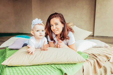 Obraz na płótnie Canvas Young mother holding her child. Woman and infant little girl relaxing in white light bedroom indoors. Happy family at home. Young mom playing whith her daughter.