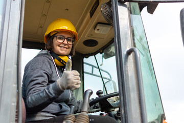 cheerful female excavator operator on construction site. Woman construction apprentice learning to drive heavy equipment - obrazy, fototapety, plakaty