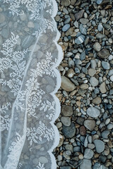 White floral boho vintage lace curtain lying on the river with a lot of small stones. Used as background or textures.