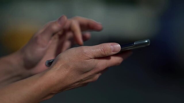 woman is surfing internet by smartphone, using apps and social nets, closeup of hands outdoors