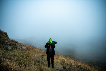 a tourist with a camera on a mountainside against the backdrop of fog and sunset