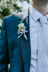 Happy groom with fresh beautiful elegant floral boutonniere on his blue wedding suit. Green background.